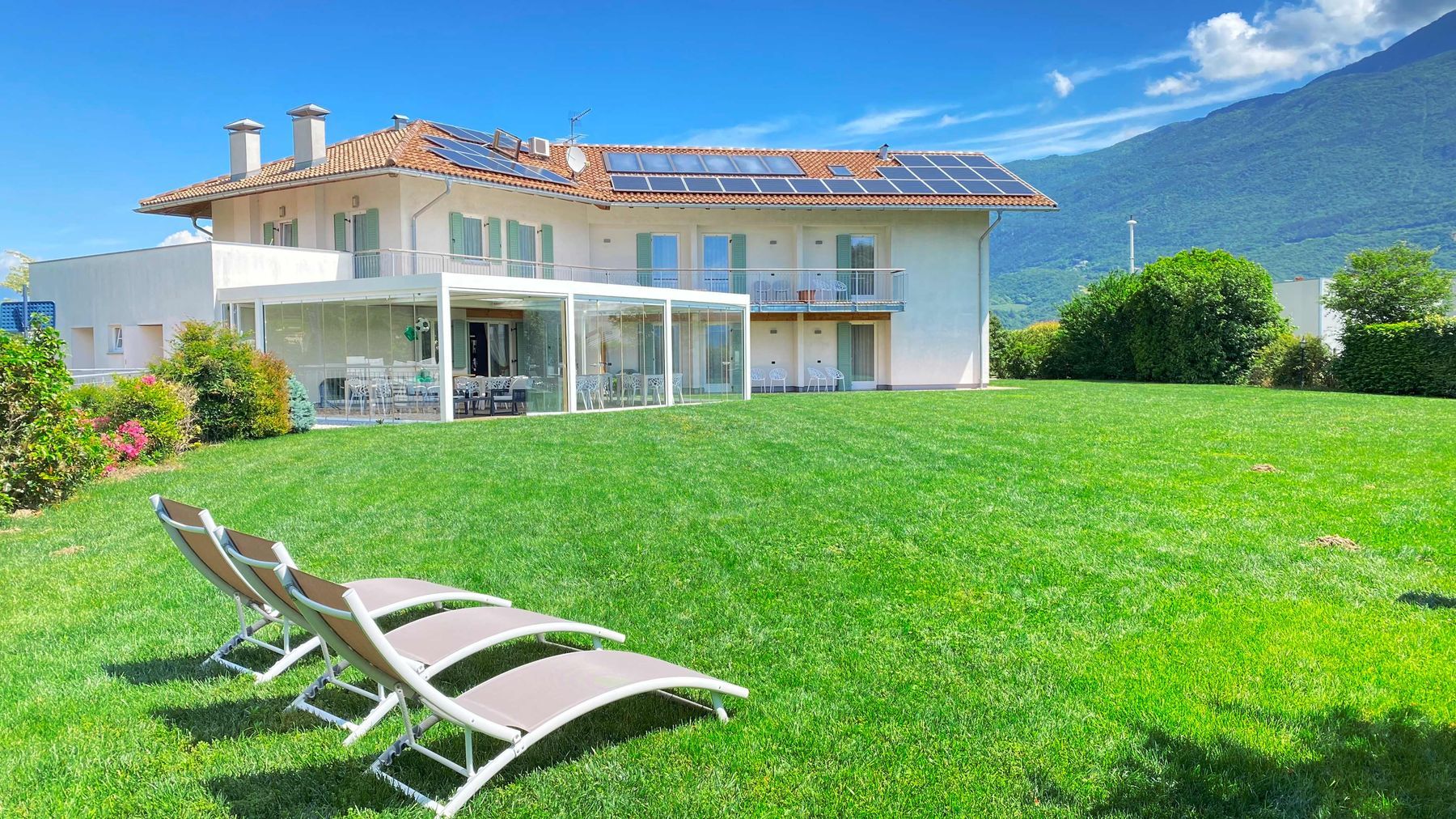 La casa della Locanda con il prato e le sdraio, sullo sfondo le montagne